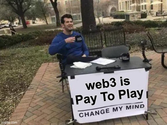 Homem com café, sentando em uma mesa com um cartaz onde se lê: 'web3 is pay to play. Change my Mind' — web 3 é pay to play. Mude minha opinião.